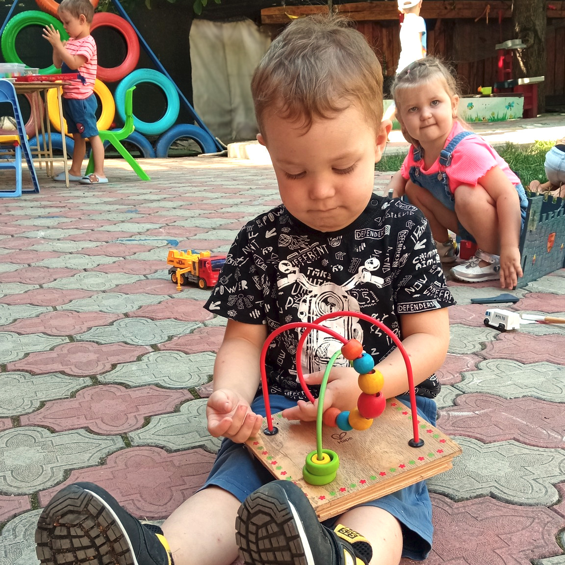 Băiețel concentrat la labirint cu mărgele, în curtea grădiniței