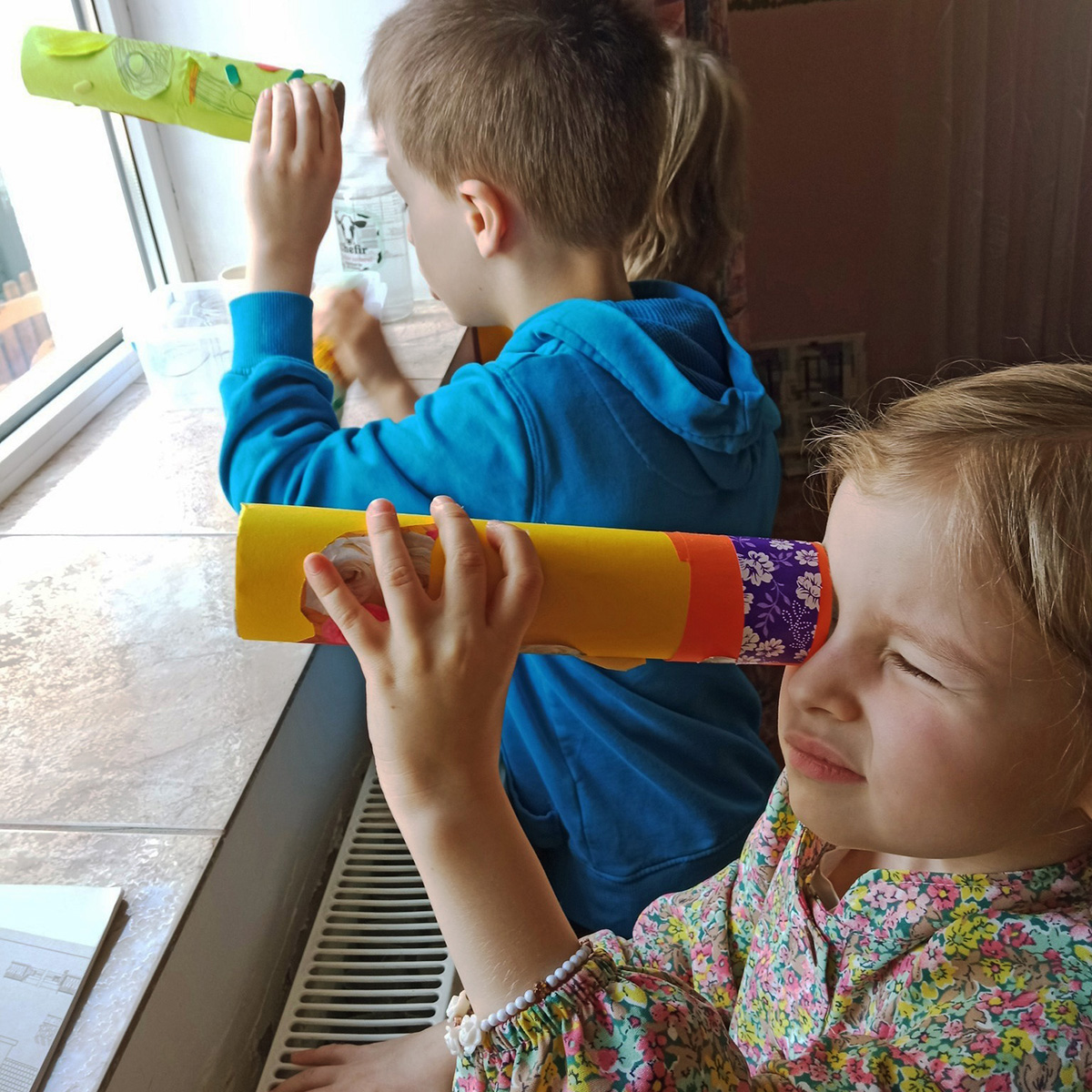 Copii explorând cu telescoape artizanale la fereastră