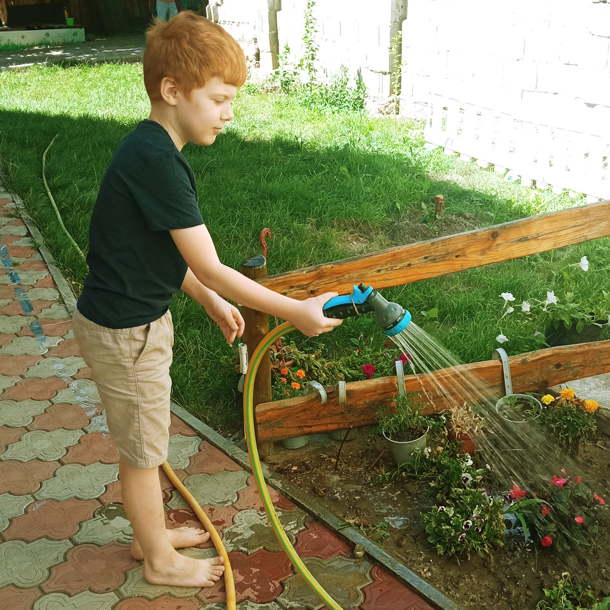 Băiat udă grădina de flori cu furtunul