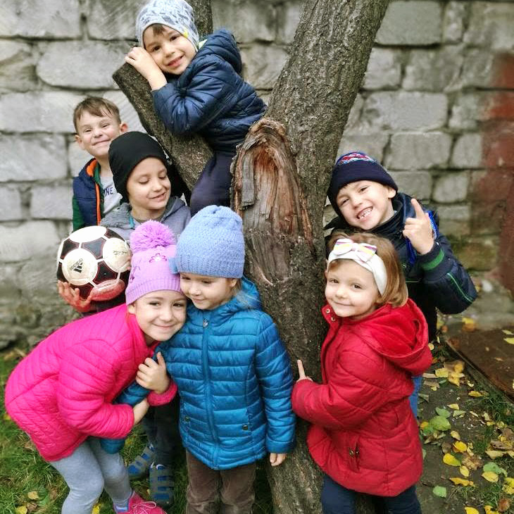 Grup de copii zâmbitori pozează lângă un copac