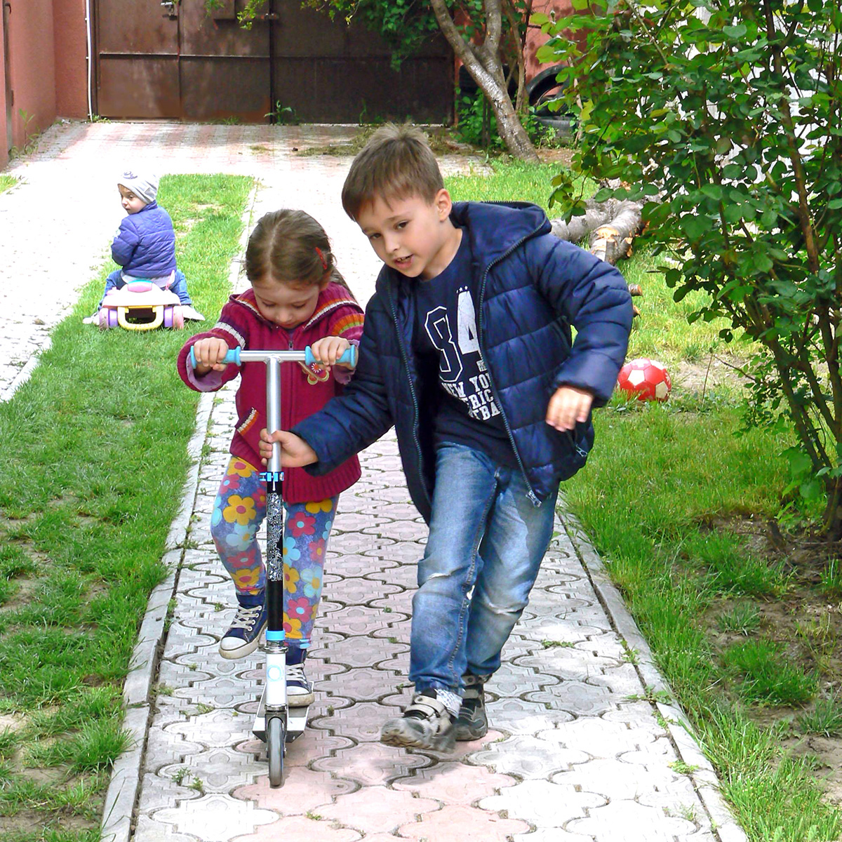 Băiat mai mare ajută unei fetițe să meargă pe trotinetă