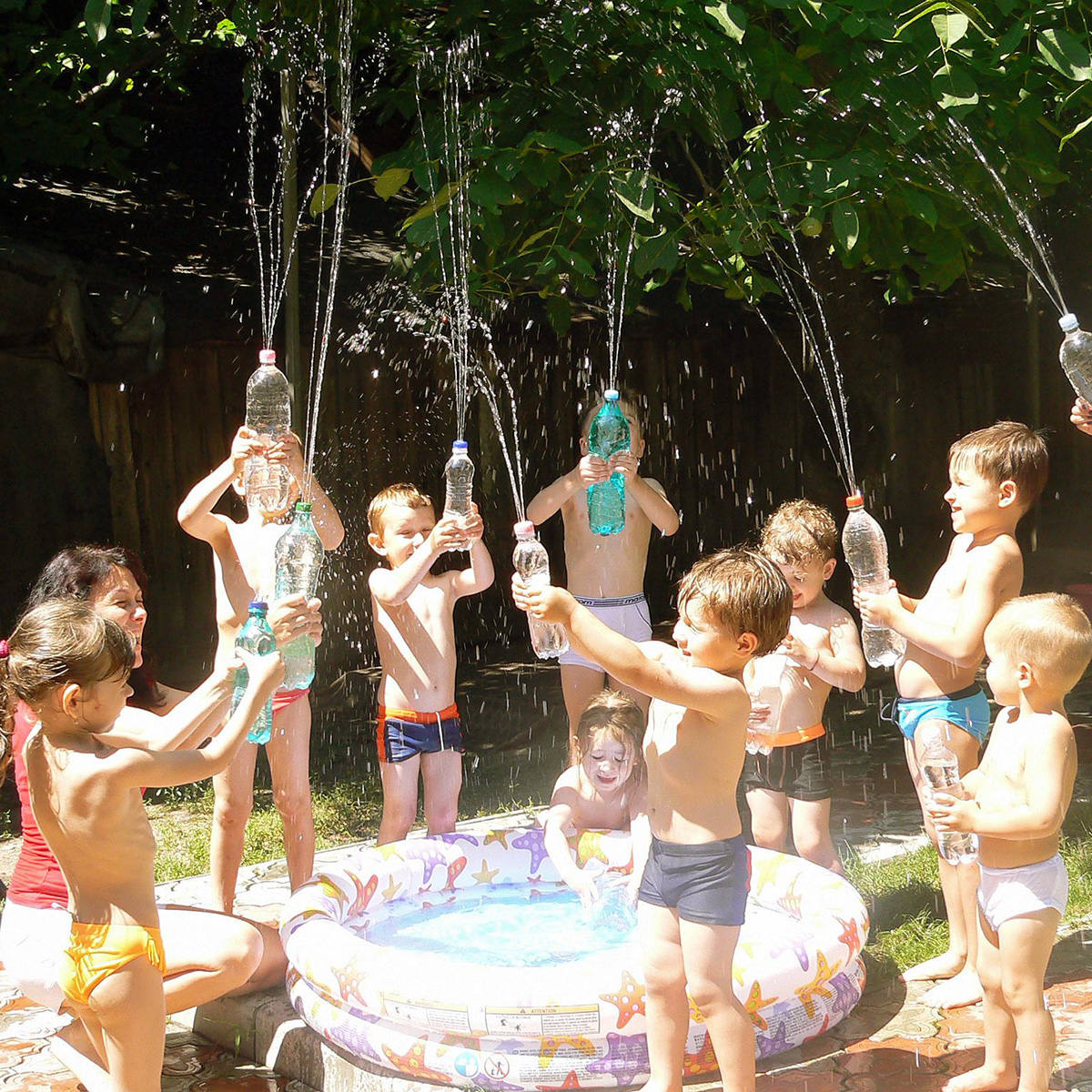 Joacă cu apă: copii stropesc cu sticle lângă o piscină gonflabilă